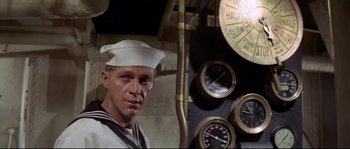 Movie still from “The Sand Pebbles” (1966), directed by Robert Wise – A man in a sailor's uniform standing in front of a clock; Close Up shot, Low angle