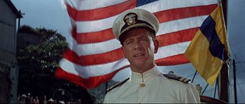 Movie still from “The Sand Pebbles” (1966), directed by Robert Wise – A man in a uniform standing in front of an american flag; Close Up shot, Low angle