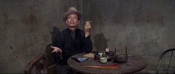 Movie still from “The Sand Pebbles” (1966), directed by Robert Wise – A man sitting at a table holding a piece of food; Medium shot, High angle
