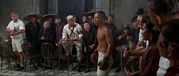 Movie still from “The Sand Pebbles” (1966), directed by Robert Wise – A group of people standing around a man with boxing mitts on; Wide shot, High angle