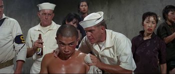 Movie still from “The Sand Pebbles” (1966), directed by Robert Wise – A man is shaving another man's head in a uniform; Medium shot, Over the shoulder angle