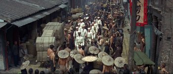 Movie still from “The Sand Pebbles” (1966), directed by Robert Wise – A group of people walking down a street with umbrellas on their heads; Extreme Wide shot, High angle