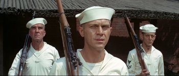 Movie still from “The Sand Pebbles” (1966), directed by Robert Wise – A man holding a rifle in front of a brick building; Close Up shot, Low angle