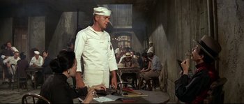 Movie still from “The Sand Pebbles” (1966), directed by Robert Wise – A man wearing a sailor's uniform standing in front of a table; Medium shot, Over the shoulder angle