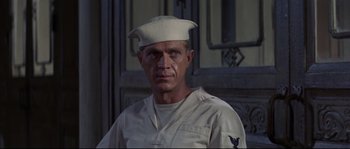 Movie still from “The Sand Pebbles” (1966), directed by Robert Wise – A man wearing a sailor's hat in front of a building; Close Up shot, Over the shoulder angle