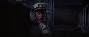 Movie still from “The Sand Pebbles” (1966), directed by Robert Wise – A man in a uniform standing next to a wall; Medium shot, Low angle