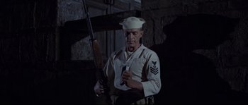 Movie still from “The Sand Pebbles” (1966), directed by Robert Wise – A man holding a rifle in front of a brick wall; Medium shot, Low angle