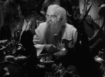 Movie still from “The Scarlet Empress” (1934), directed by Josef von Sternberg – An old man with long white beard sitting at a table; Medium shot, High angle
