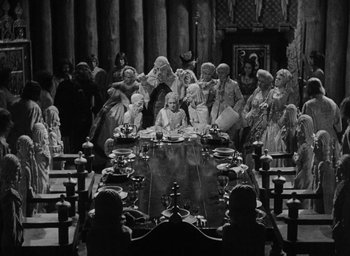 Movie still from “The Scarlet Empress” (1934), directed by Josef von Sternberg – A black and white photo of a group of people sitting around a table; Extreme Wide shot, High angle