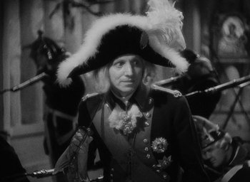 Movie still from “The Scarlet Empress” (1934), directed by Josef von Sternberg – A man wearing a hat with feathers on top of his head; Medium shot, High angle