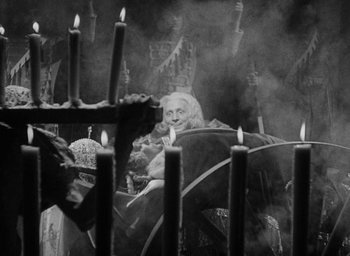 Movie still from “The Scarlet Empress” (1934), directed by Josef von Sternberg – An old man sitting in front of a bunch of lit candles; Medium shot, High angle