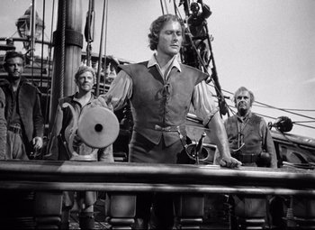 Movie still from “The Sea Hawk” (1940), directed by Michael Curtiz – A man standing next to another man on top of a boat; Medium shot, Low angle