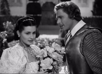 Movie still from “The Sea Hawk” (1940), directed by Michael Curtiz – A man and a woman standing next to each other holding flowers; Medium shot, High angle