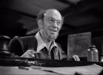 Movie still from “The Sea Hawk” (1940), directed by Michael Curtiz – An older man sitting at a table with a pen in his mouth; Close Up shot, Low angle