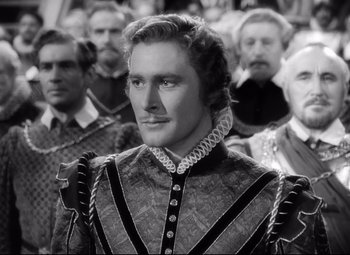 Movie still from “The Sea Hawk” (1940), directed by Michael Curtiz – A black and white photo of a man in a crowd; Medium shot, Over the shoulder angle