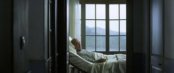 Movie still from “The Sea Inside” (2004), directed by Alejandro Amenábar – A man laying in a bed in a room with a mountain view; Medium shot, Low angle