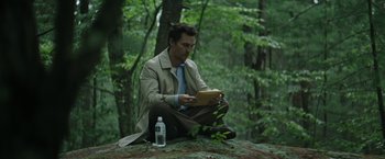 Movie still from “The Sea of Trees” (2015), directed by Gus Van Sant – A man sitting on the ground in the woods looking at a tablet computer; Medium shot, Low angle
