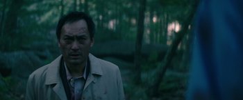 Movie still from “The Sea of Trees” (2015), directed by Gus Van Sant – A man in a white jacket standing in the woods; Close Up shot, Over the shoulder angle