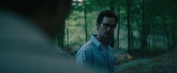 Movie still from “The Sea of Trees” (2015), directed by Gus Van Sant – A man with glasses standing in the woods; Close Up shot, Over the shoulder angle