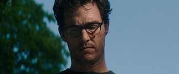 Movie still from “The Sea of Trees” (2015), directed by Gus Van Sant – A person wearing glasses with trees in the background; Close Up shot, Low angle
