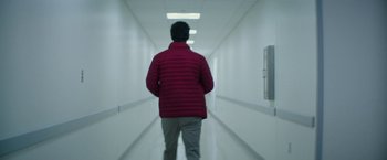 Movie still from “The Sea of Trees” (2015), directed by Gus Van Sant – A man wearing a red jacket walking down a hallway; Medium shot, Low angle