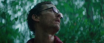 Movie still from “The Sea of Trees” (2015), directed by Gus Van Sant – A person wearing glasses with trees in the background; Close Up shot, Low angle