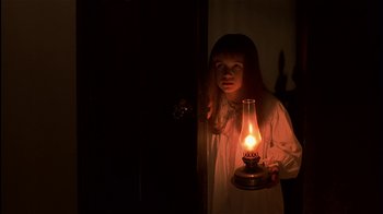 Movie still from “The Secret Garden” (1993), directed by Agnieszka Holland – A little girl standing in a dark room holding an oil lamp; Medium shot, High angle