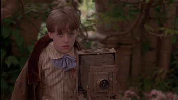 Movie still from “The Secret Garden” (1993), directed by Agnieszka Holland – A young boy holding an old camera in a wooded area; Close Up shot, Low angle