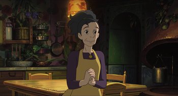 Movie still from “The Secret World of Arrietty” (2010), directed by Hiromasa Yonebayashi – An animated woman in a yellow and purple apron is standing in front of a wooden table; Medium shot, High angle
