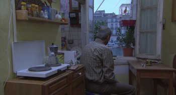 Movie still from “The Secret of the Grain” (2007), directed by Abdellatif Kechiche – An older man sitting in front of a kitchen window; Wide shot, High angle
