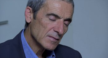 Movie still from “The Secret of the Grain” (2007), directed by Abdellatif Kechiche – An older man wearing a blue shirt and a black jacket; Close Up shot, Over the shoulder angle