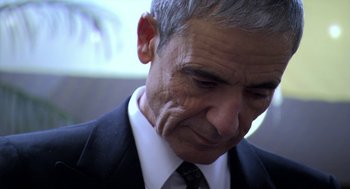 Movie still from “The Secret of the Grain” (2007), directed by Abdellatif Kechiche – An older man wearing a suit and tie; Close Up shot, Over the shoulder angle