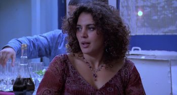 Movie still from “The Secret of the Grain” (2007), directed by Abdellatif Kechiche – A person with curly hair sitting at a table; Close Up shot, Over the shoulder angle