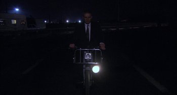 Movie still from “The Secret of the Grain” (2007), directed by Abdellatif Kechiche – A man in a suit riding a bicycle at night; Wide shot, Low angle