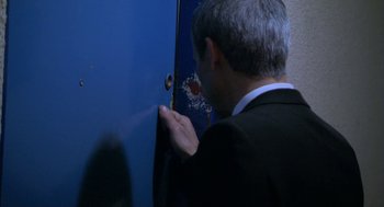 Movie still from “The Secret of the Grain” (2007), directed by Abdellatif Kechiche – A man in a black suit and white shirt looking into a blue door; Close Up shot, High angle