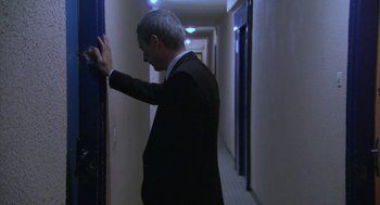 Movie still from “The Secret of the Grain” (2007), directed by Abdellatif Kechiche – A man in a suit and tie leaning against a wall; Medium shot, Over the shoulder angle