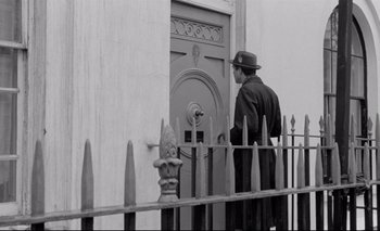 Movie still from “The Servant” (1963), directed by Joseph Losey – A black and white photo of a man in a hat; Wide shot, Low angle