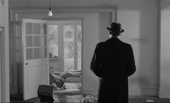 Movie still from “The Servant” (1963), directed by Joseph Losey – A black and white photo of a man in a hat looking out a door; Wide shot, Over the shoulder angle