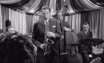 Movie still from “The Servant” (1963), directed by Joseph Losey – A man holding a saxophone while standing next to another man playing a contrabass; Medium shot, Low angle