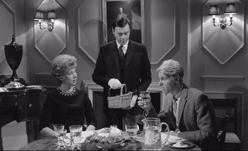 Movie still from “The Servant” (1963), directed by Joseph Losey – A black and white photo of a man and two women at a dinner table; Medium shot, Over the shoulder angle