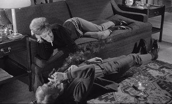 Movie still from “The Servant” (1963), directed by Joseph Losey – A man and a woman are laying on the couch smoking; Wide shot, High angle