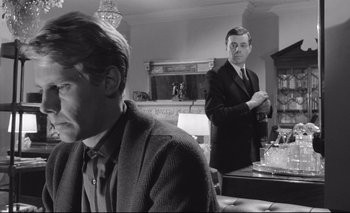 Movie still from “The Servant” (1963), directed by Joseph Losey – A man standing in front of another man in a room; Medium shot, Over the shoulder angle