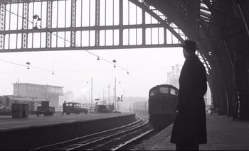 Movie still from “The Servant” (1963), directed by Joseph Losey – A man standing on a train platform next to a train; Wide shot, Low angle