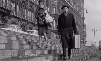 Movie still from “The Servant” (1963), directed by Joseph Losey – An old photo of a man and a woman walking down the stairs; Wide shot, Low angle