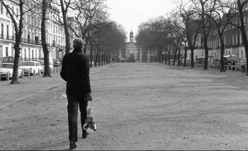 Movie still from “The Servant” (1963), directed by Joseph Losey – A man walking down a street holding a bag; Wide shot, Low angle