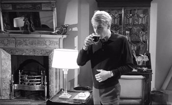 Movie still from “The Servant” (1963), directed by Joseph Losey – A man drinking a glass of wine in a living room; Medium shot, High angle
