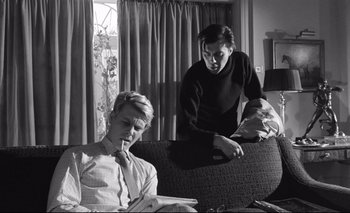 Movie still from “The Servant” (1963), directed by Joseph Losey – A man and a woman sitting on a couch looking at a book; Medium shot, Low angle