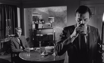 Movie still from “The Servant” (1963), directed by Joseph Losey – A man drinking a glass of wine at a dinner table; Medium shot, Over the shoulder angle