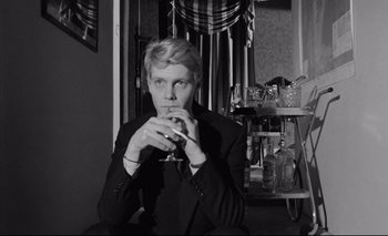 Movie still from “The Servant” (1963), directed by Joseph Losey – Black and white photograph of a man smoking a cigarette; Medium shot, Low angle