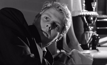 Movie still from “The Servant” (1963), directed by Joseph Losey – Black and white photograph of a man in a suit and tie; Close Up shot, Low angle